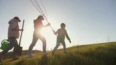 Bir aile akşam güneşine karşı bir fidan ve bahçe aletleriyle tepeye tırmanır, ortak emeği ve doğayı sembolize eder.