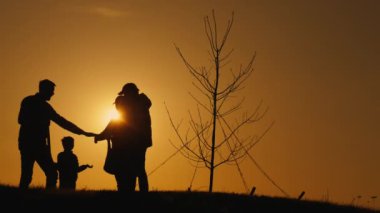 Gün batımında bir ailenin silueti ağaç dikilirken, nesiller arası bağlantıyı ve doğayla ilgilenmeyi sembolize eder.