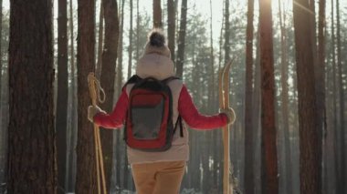 Sırt çantalı bir kadın kayaklarıyla karlı bir ormanda duruyor. Açık hava aktivitelerine hazır.
