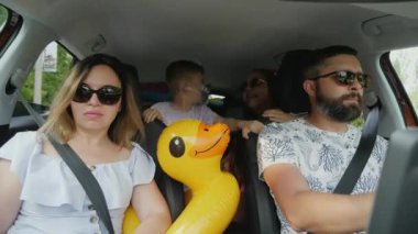 Çocuklar arabada arka koltuklarda otururken deniz seyahatinde mutlu olurlar. Ciddi ebeveynler önde oturur, babalar arabayı sürer.