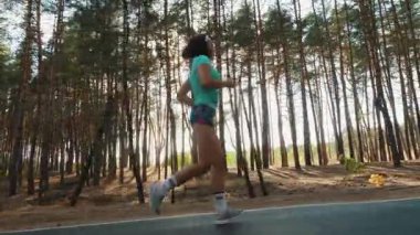 Uzun çam ağaçlarıyla çevrili orman yolunda koşan spor giyimli aktif bir kadın. Sağlıklı yaşam tarzı, dayanıklılık ve doğa koşulları.