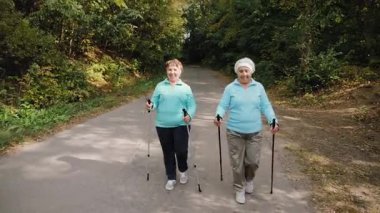 İki aktif son sınıf öğrencisi, ormanda sırıkla yürüyor. Sağlıklı yaşam tarzı, açık hava aktivitesi ve yaşlı yetişkinler için uygunluk.