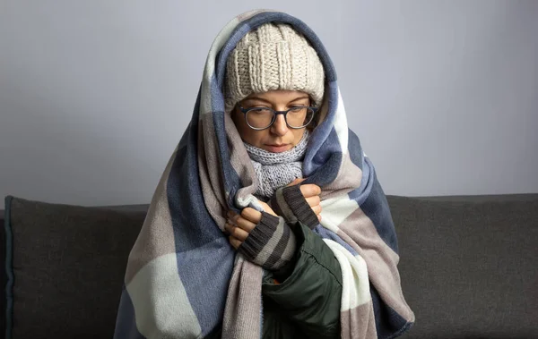 冬の寒い部屋に座っている間に毛布に包まれた女性は暖まる ストックフォト