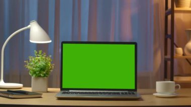 Aydınlatılmış modern odada masaüstünde yeşil ekranlı dizüstü bilgisayar.