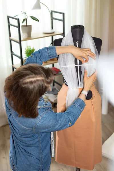 Seamstress tailor works with fabric for sewing designer clothes using a mannequin.