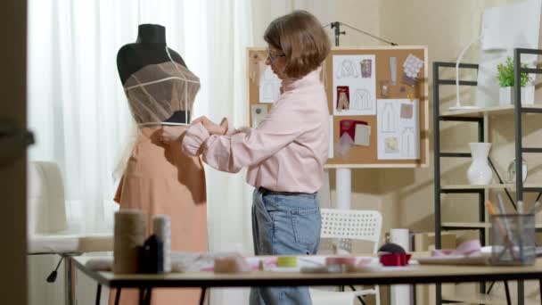 ファッションデザイナーの女性がスタジオで働いている間にファブリックとマネキンを使って服を作る — ストック動画