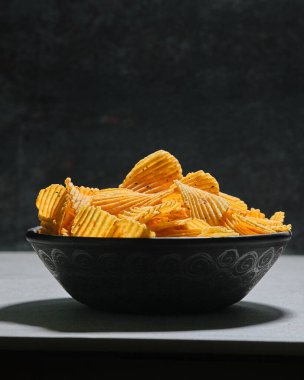 Koyu arkaplanda büyük bir kase dalgalı patates cipsi..
