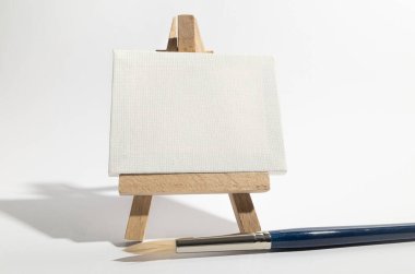 Boş tuval ve boya fırçası olan küçük tahta sehpa..