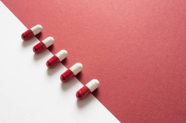 Kırmızı kağıdın arka planında kırmızı ve beyaz hapların yakın plan çekimi. Sağlık ve Tıp Konsepti.