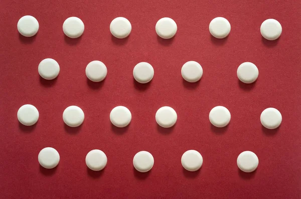 white pills, tablets and a large pill on an abstract red, background, close-up