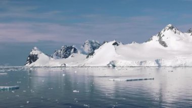 Karlı dağlarla, buzullarla ve buzdağlarıyla Antarktika manzarası. Antarktika 'daki buzlu kıyıların manzarası. Aynadaki yansıması okyanusta yüzen güzel mavi buzdağı. Sert bir kıtanın buzulları