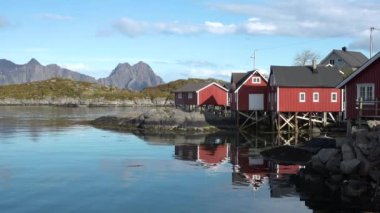 Kırmızı evleri olan küçük bir balıkçı köyünün manzarası. Beyaz karla kaplı güzel dağlar. Lofoten Adası, Norveç. Fiyort kıyısındaki kır evi. Geleneksel ahşap balıkçıların evleri..