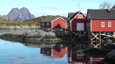 Kırmızı evleri olan küçük bir balıkçı köyünün manzarası. Beyaz karla kaplı güzel dağlar. Lofoten Adası, Norveç. Fiyort kıyısındaki kır evi. Geleneksel ahşap balıkçıların evleri..
