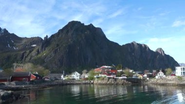 Kırmızı evleri olan küçük bir balıkçı köyünün manzarası. Beyaz karla kaplı güzel dağlar. Lofoten Adası, Norveç. Fiyort kıyısındaki kır evi. Geleneksel ahşap balıkçıların evleri..
