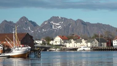 Kırmızı evleri olan küçük bir balıkçı köyünün manzarası. Beyaz karla kaplı güzel dağlar. Lofoten Adası, Norveç. Fiyort kıyısındaki kır evi. Geleneksel ahşap balıkçıların evleri..