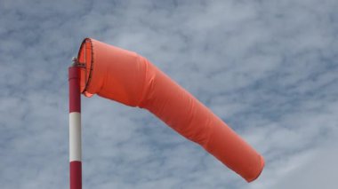 Rüzgâr Sock rüzgar yönünü ve hızı göstermek için rüzgarda esiyor. Arka planda bulutlu gökyüzü olan rüzgârlı bir çorap. Rüzgarın yönü ve hızı için temel rehber olarak kullanılan kumaş konik tüp.