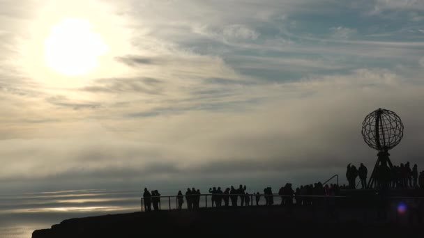 カラフルな雲とグローブモニュメントと人々のシルエットでサンセットのノルドカップ ノルウェーのマゼロヤ島 真夜中にノースケープのグローブモニュメント — ストック動画