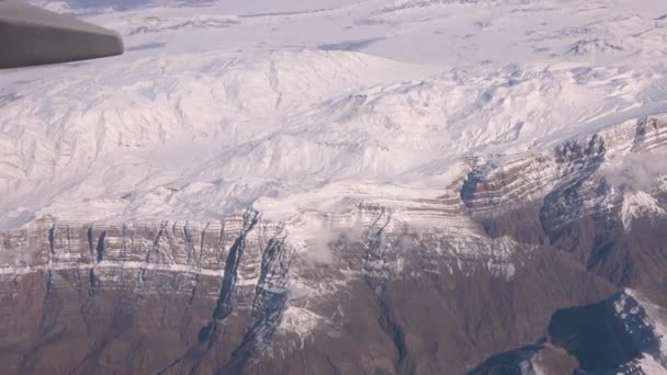 飛行機の窓から山が撃たれた 雪は冬の山の谷を覆いました ランドスケープ シアタービュー 飛行機の窓から見たショット — ストック動画