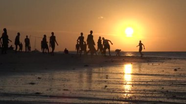 İnsanlar plaj futbolu oynuyor. Plaj futbolu oynayan gençlerin siluetleri. Gençler gün batımında okyanus kıyısında plaj futbolu oynuyorlar. Sağlıklı yaşam tarzı kavramı
