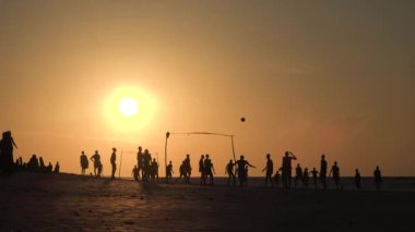 İnsanlar plaj futbolu oynuyor. Plaj futbolu oynayan gençlerin siluetleri. Gençler gün batımında okyanus kıyısında plaj futbolu oynuyorlar. Sağlıklı yaşam tarzı kavramı