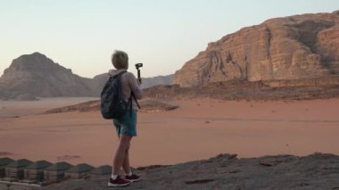Seyahat ve macera. Günbatımı gezisindeki kadın turist çöldeki manzaraların fotoğrafını çekiyor. Wadi Rom Çölü 'nde çölde gün doğumu turu. Genç bayan yürüyüşçü doğa çöl manzarasının tadını çıkarıyor..