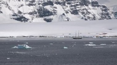 Buz kıyıları arasında donmuş kış sularında yüzen bir tekne. Etrafı buzdağlarıyla çevrili okyanusta bir tekne gezisi. Antarktika okyanusunda bir tekne. Turizm, Antarktika Yarımadasını keşfetmek.