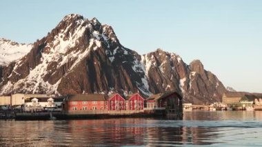 Lofoten Adaları 'ndaki kırmızı ahşap Rorbu kulübeleri. Geleneksel balıkçı köyü, karlı bölgelere karşı kırmızı rorbu evleri. Huzurlu manzara suya güzel bir şekilde yansıyor. Norveç.