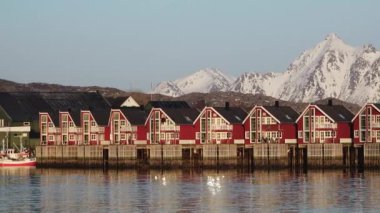 Lofoten Adaları 'ndaki kırmızı ahşap Rorbu kulübeleri. Geleneksel balıkçı köyü, karlı bölgelere karşı kırmızı rorbu evleri. Huzurlu manzara suya güzel bir şekilde yansıyor. Norveç.