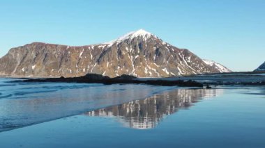 İnanılmaz bir seyahat. Deniz kıyısının uçan insansız hava aracı, karlı dağlar, kışın gün batımında daha da beter. Lofoten Adaları, Norveç. Fiyort, köy, sudaki yansıma, kayalar....