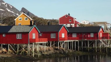 Sudaki yansıma. Karlı dağlar, balıkçı köyü. Okyanustaki parlak kırmızı evler. Norveç 'teki Lofoten adaları. Tipik kırmızı kulübeleriyle popüler bir turizm merkezi. Norveç rorbu 'su.