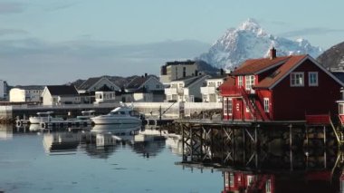Sudaki yansıma. Karlı dağlar, balıkçı köyü. Okyanustaki parlak kırmızı evler. Norveç 'teki Lofoten adaları. Tipik kırmızı kulübeleriyle popüler bir turizm merkezi. Norveç rorbu 'su.