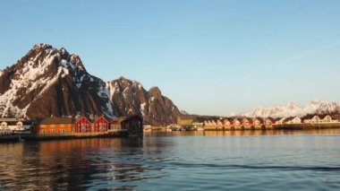 Sudaki yansıma. Karlı dağlar, balıkçı köyü. Okyanustaki parlak kırmızı evler. Norveç 'teki Lofoten adaları. Tipik kırmızı kulübeleriyle popüler bir turizm merkezi. Norveç rorbu 'su.