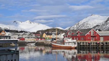 Sudaki yansıma. Karlı dağlar, balıkçı köyü. Okyanustaki parlak kırmızı evler. Norveç 'teki Lofoten adaları. Tipik kırmızı kulübeleriyle popüler bir turizm merkezi. Norveç rorbu 'su.
