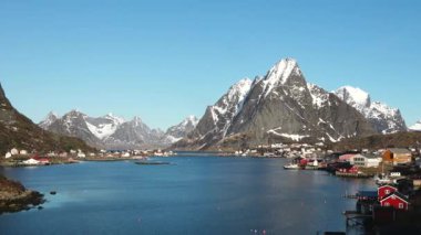 Sudaki yansıma. Karlı dağlar, balıkçı köyü. Okyanustaki parlak kırmızı evler. Norveç 'teki Lofoten adaları. Tipik kırmızı kulübeleriyle popüler bir turizm merkezi. Norveç rorbu 'su.