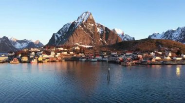 İnanılmaz bir seyahat. Deniz kıyısının uçan insansız hava aracı, karlı dağlar, kışın gün batımında daha da beter. Lofoten Adaları, Norveç. Fiyort, köy, sudaki yansıma, kayalar....