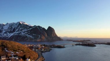 İnanılmaz bir seyahat. Deniz kıyısının uçan insansız hava aracı, karlı dağlar, kışın gün batımında daha da beter. Lofoten Adaları, Norveç. Fiyort, köy, sudaki yansıma, kayalar....