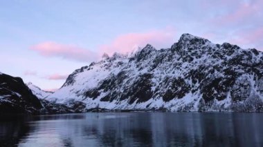 Norveç. Beyaz karla kaplı yüksek dağlı kayalık tepelerin nefes kesici manzarası. Kışın Lofoten fiyortlarının panoramik manzarası, doğanın sakin güzelliği..