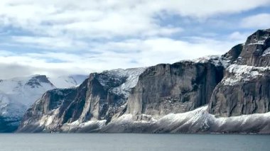 Kar, sakin bir deniz boyunca uzanan dramatik uçurumları örterek, sakin kutup ortamını yansıtır. Bu çarpıcı manzara uzak bir yerde kışın ihtişamını yansıtıyor..
