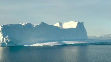 Buzdağları Grönland 'da gün batımında dağlarla çevrili bir buzulun sakin sularında yüzer.