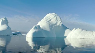 Buzdağları sakin sularda soluk kesici Kuzey Kutbu çevresiyle sarılı bir şekilde sürüklenirler. Gökyüzü açık, doğanın güzelliğini en iyi şekilde gösteriyor..