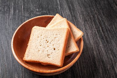 Üç dilim taze ekmek yuvarlak ahşap bir kasede, koyu ahşap bir masada, kahvaltı ya da hafif bir aperatif için mükemmel. Basit sunum ekmeğin dokusunu vurgular.