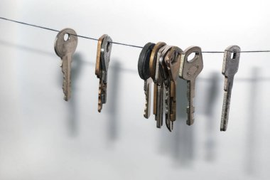 İpe asılmış farklı kilitlerden farklı anahtarlar. Beyaz bir duvarda bir damla gölge var.