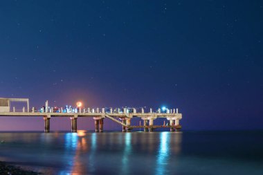 İskelede gece balıkçılığı, balıkçılarla iskelede ay ışığı, yıldızlı bir arka plan.  