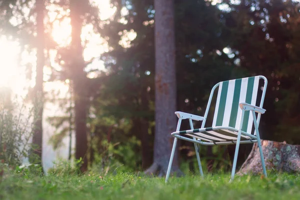 stock image Empty folding camp chair for relaxing on the field near the forest with blurred sunset background