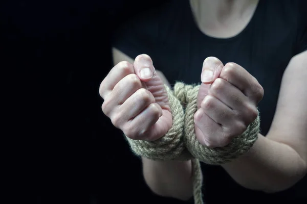 Hands of a victim woman tied up with rough rope on the black background. Stop abusing violence concept