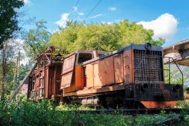 Eski paslı turuncu dizel lokomotif. Demiryolunda kırık ahşap yük vagonu var.