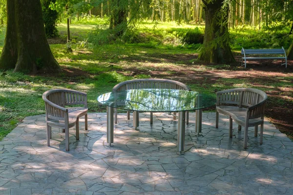 Empty garden furniture with glass table for leisure time In park or forest. Wooden and glass outdoor furniture set for picnic