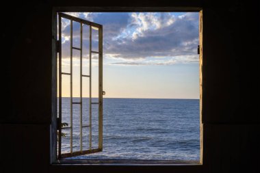 Pencereden deniz manzarası ve karanlık bir odada kafes.