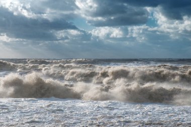 Kasırgadan sonra fırtınalı bulutlu bir gökyüzünün altında kahverengi dalgalar kıyıya vurur.