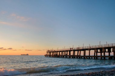 Sahilde kalabalık iskele ve ufukta bir gemi ile bir gün batımı